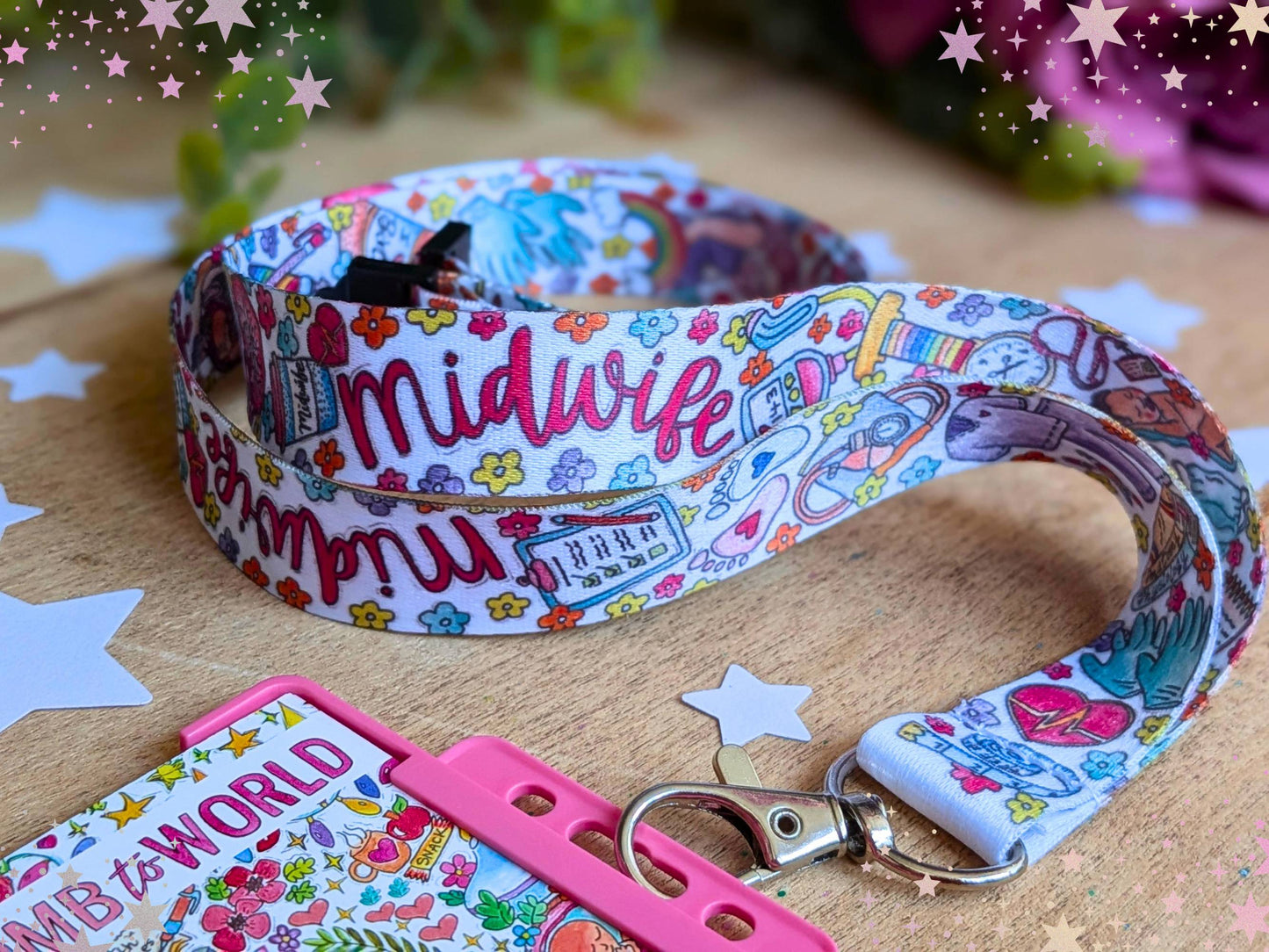 A colorful printed midwife lanyard with a matching pink card holder and clasp, displayed on a wooden surface with decorative star overlays.