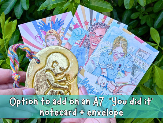 Golden baby hanging ornament with colorful braided cord and illustrated note card
